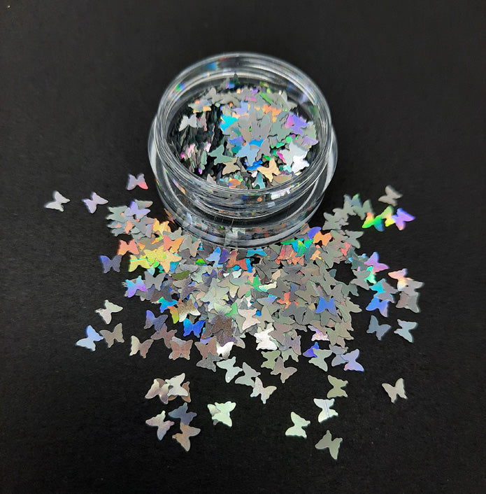 A pot of shiny silver holographic butterfly shaped sequins, used in nail art and also arts and crafts.