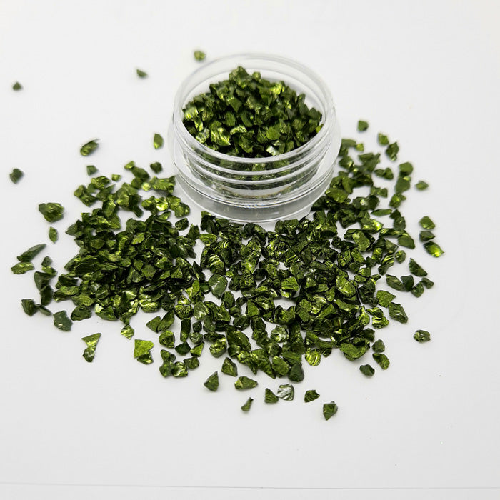 A pot of green shiny metallic irregular pieces of glass or metal. Used in nail art.