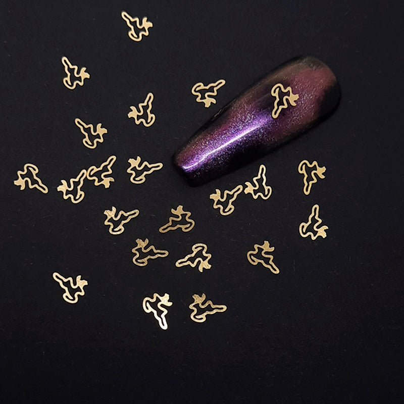 Gold deer-shaped nail art decoration on a black background with a purple glittery nail.