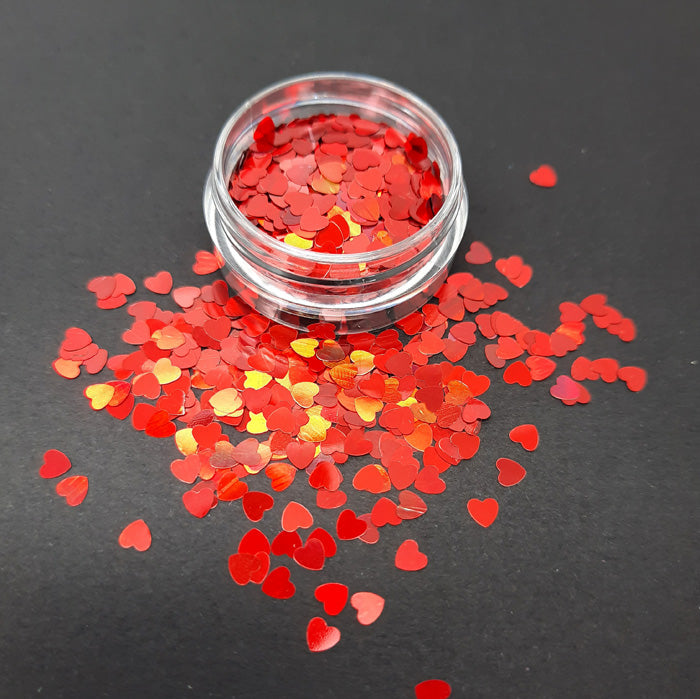 A pot of red heart shaped nail art decoration on a black background.