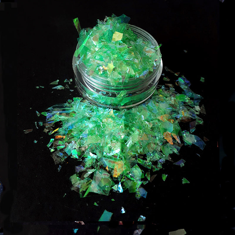 Clear container with green glittery nail flakes on a black background