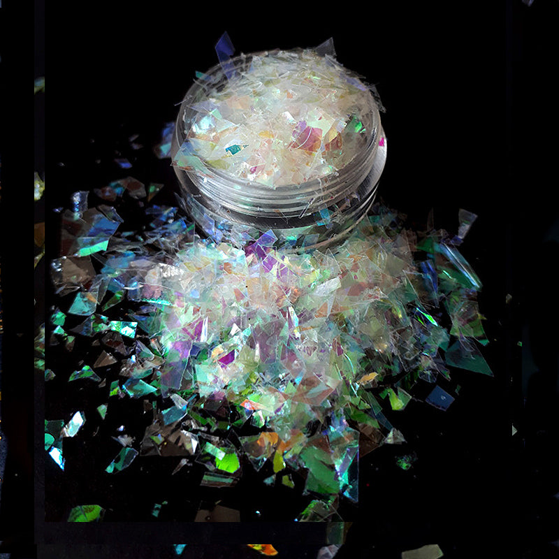 Iridescent nail flakes in a small open container on a black background