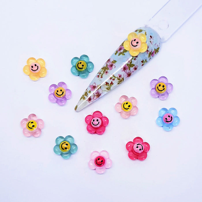 Colourful flower-shaped nail art charms with smiley faces on a white background