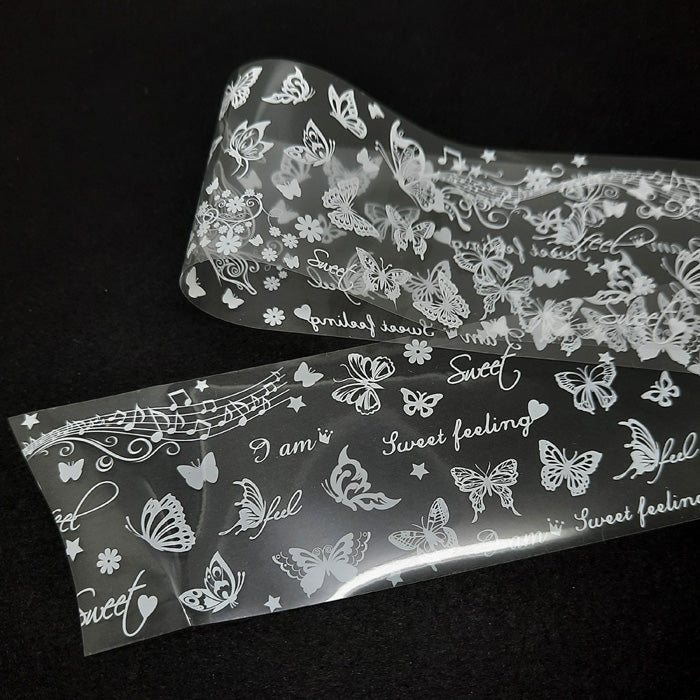 A strip of clear nail foil with a design of butterflies and music in white.