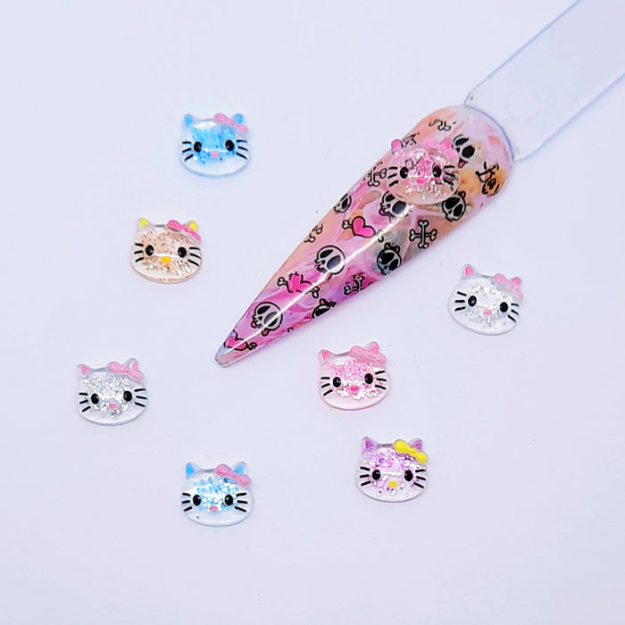 A set of colourful glittery Hello Kitty nail art charms displayed with a nail tip on a white background