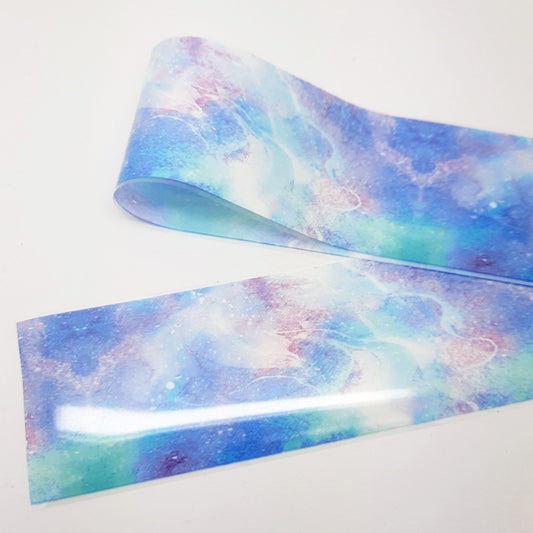 A strip of nail art foil in shades of blue, green and lilac displayed on a white background.