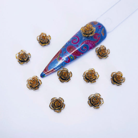 A set of gold glittery rose nail art charms with a blue nail tip on a white background