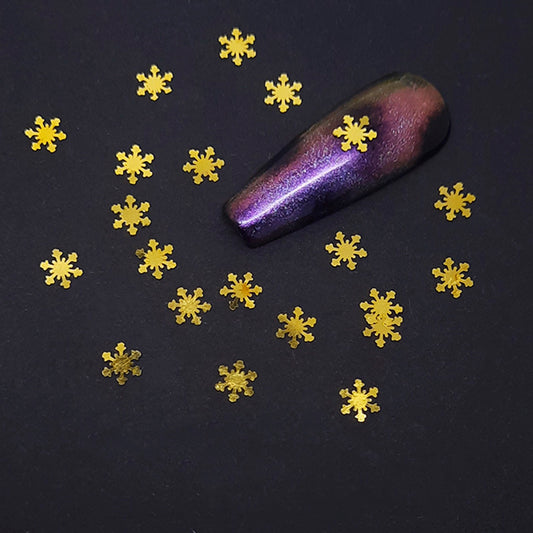 Purple glittery nail tip with gold snowflake nail decorations on a dark background