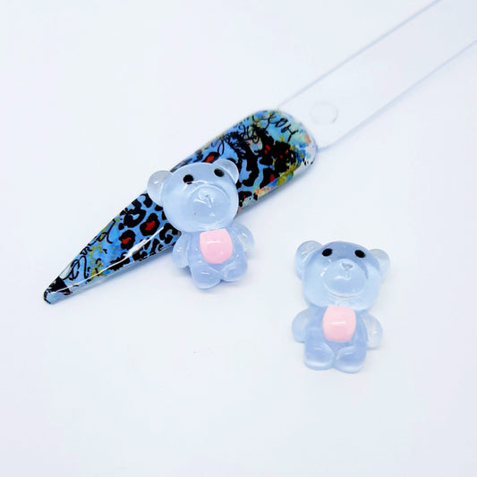 A pair of blue teddy bear nail charms displayed with a nail tip on a white background