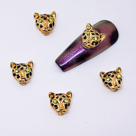 Gold leopard head nail art decorations on a purple glittery nail tip.