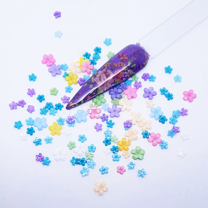 Colourful flower-shaped nail decoration scattered on a light purple background with a decorative purple nail tip.