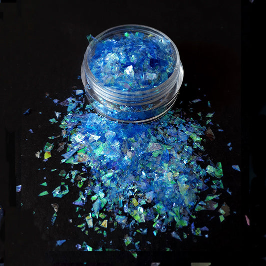 Blue nail flakes in a clear container on a black background