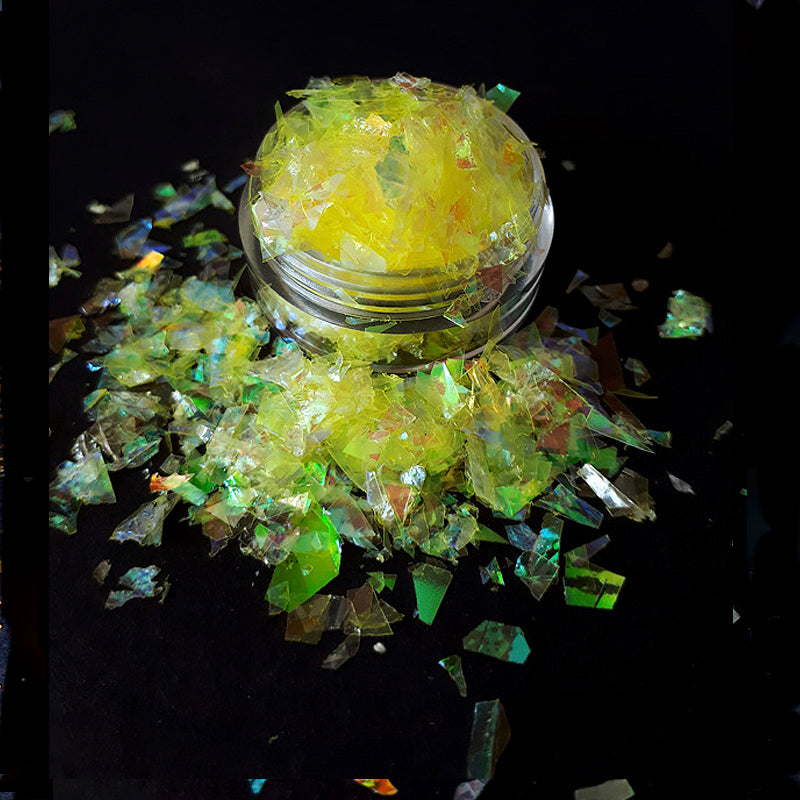 Jar of yellow mylar nail flakes with scattered pieces on a dark background