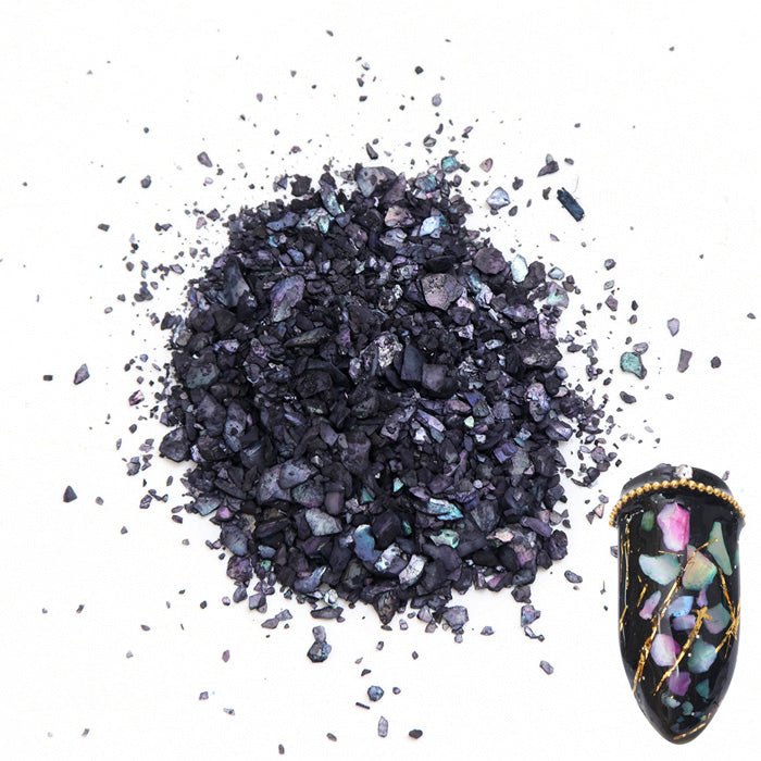 A pile of black shell flakes used in nail art displayed next to a nail tip on a white background.