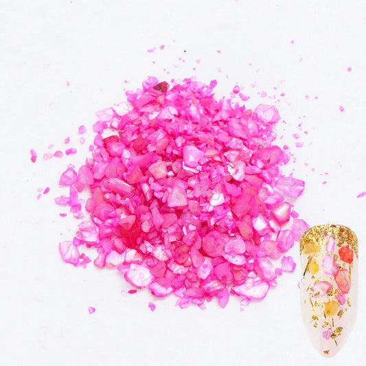 A pile of pink shell flakes used in nail art displayed next to a nail tip on a white background.