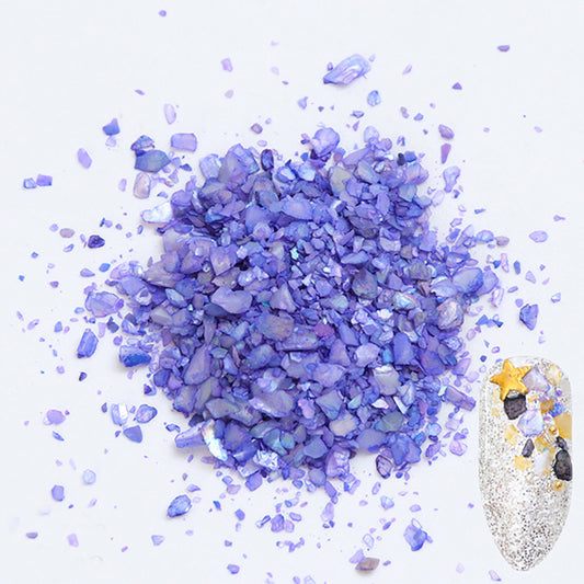 A pile of purple shell flakes used in nail art displayed next to a nail tip on a white background.