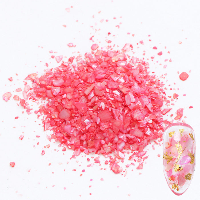 A pile of red shell flakes used in nail art displayed next to a nail tip on a white background.