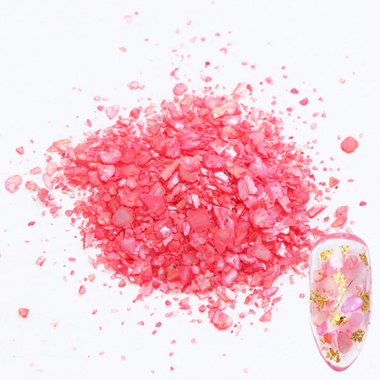 A pile of red shell flakes used in nail art displayed next to a nail tip on a white background.