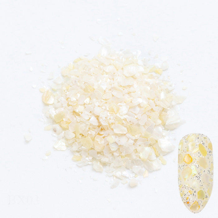 A pile of white shell flakes used in nail art displayed next to a nail tip on a white background.