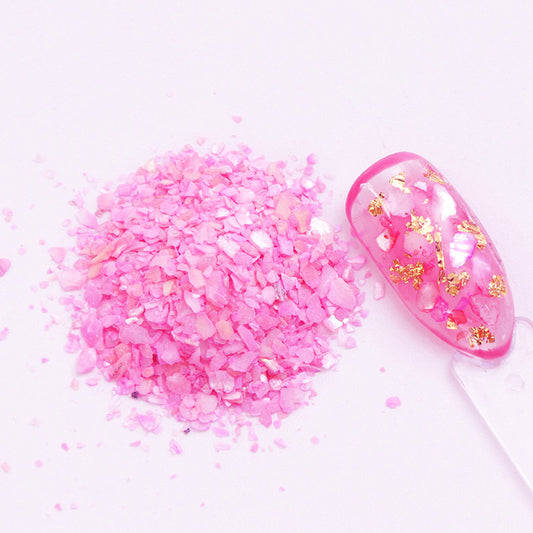 A pile of pink shell flakes used in nail art displayed next to a decorated nail tip on a white background.