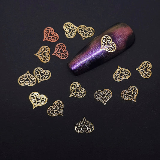Decorative heart-shaped nail art slices on a dark surface with a purple glittery nail tip.