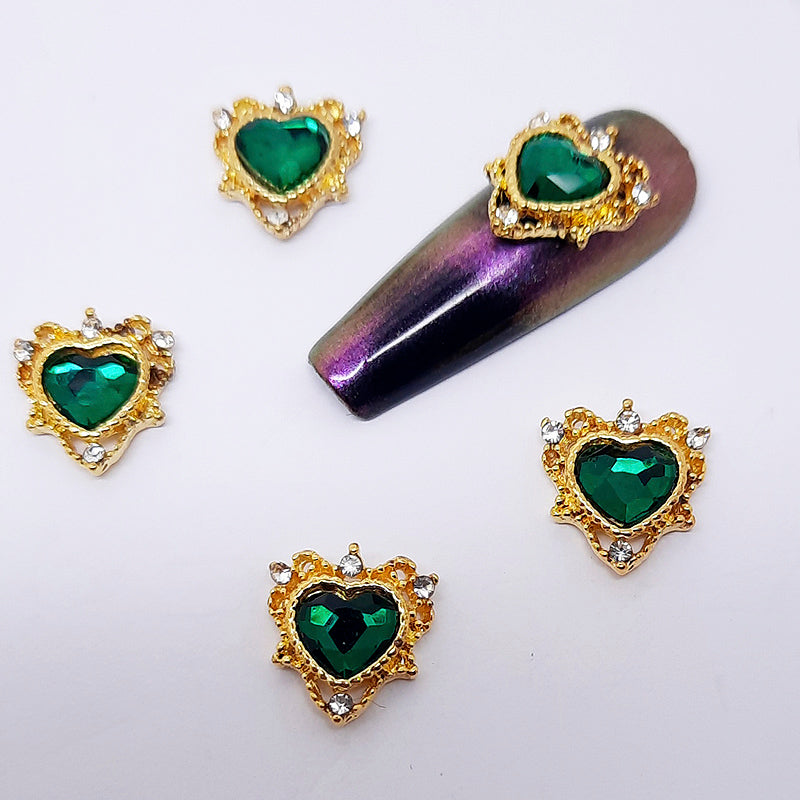 Heart shaped green crystal nail charm encased in a gold frame, shown on a nail swatch.