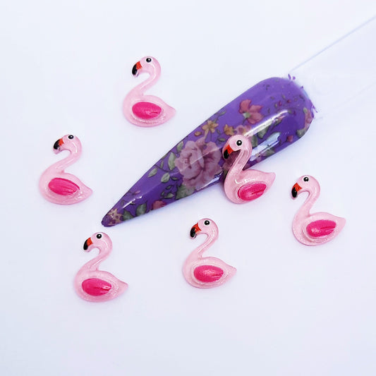 Pink flamingo-shaped nail art charms with a purple nail tip on a white background