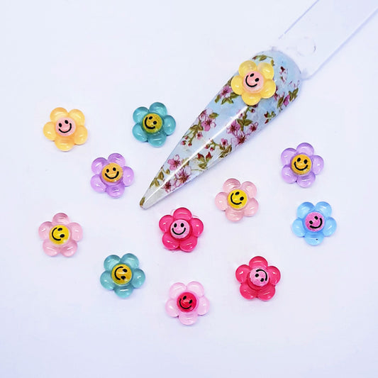 Colourful flower-shaped nail art charms with smiley faces on a white background